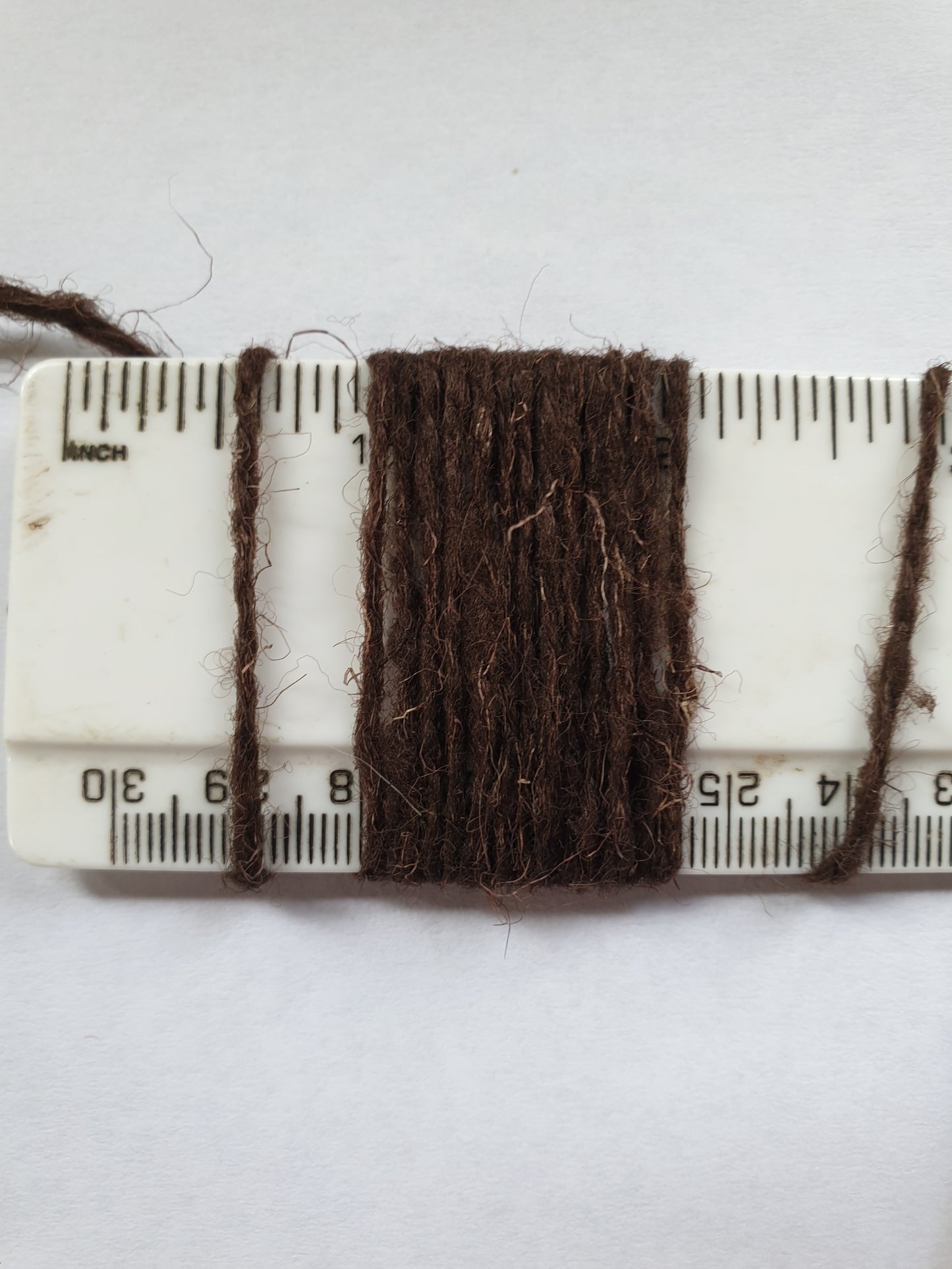 Brown rug yarn wrapped around a ruler showing wraps per inch
