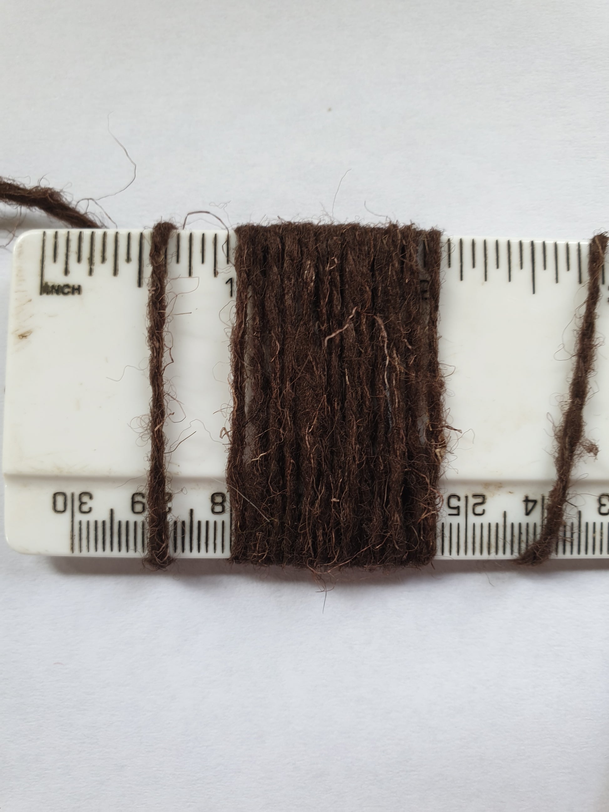 Brown rug yarn wrapped around a ruler showing wraps per inch