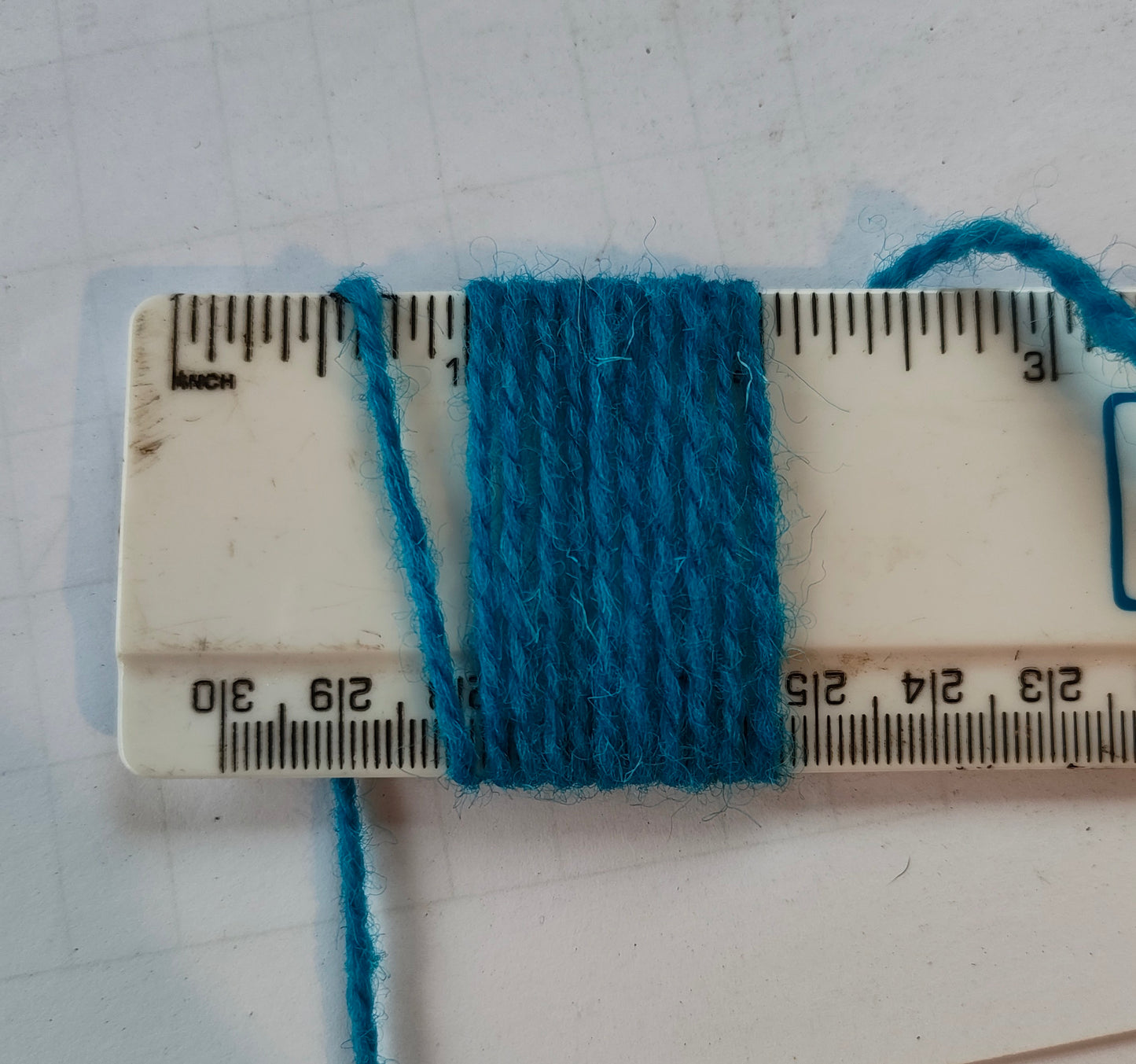 A medium thickness Turquoise blue weaving yarn showing 11 wraps per inch