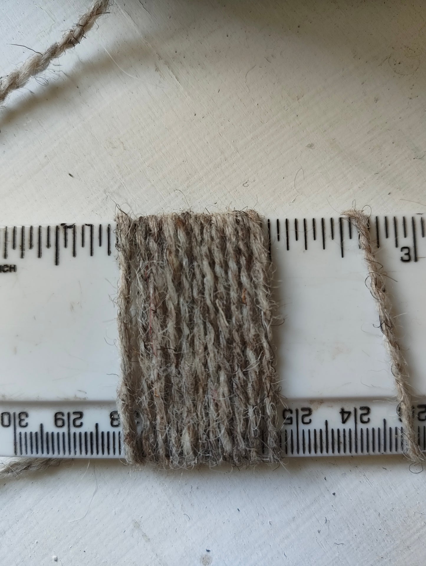 Grey tweedy pale weaving yarn showing a thickness of 11 wraps per inch