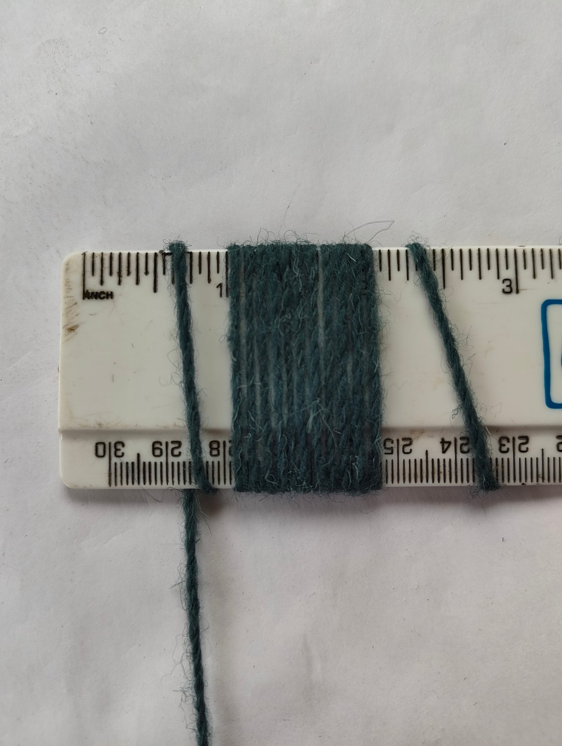 A medium thickness blue-green rug yan showing 11 wraps per inch