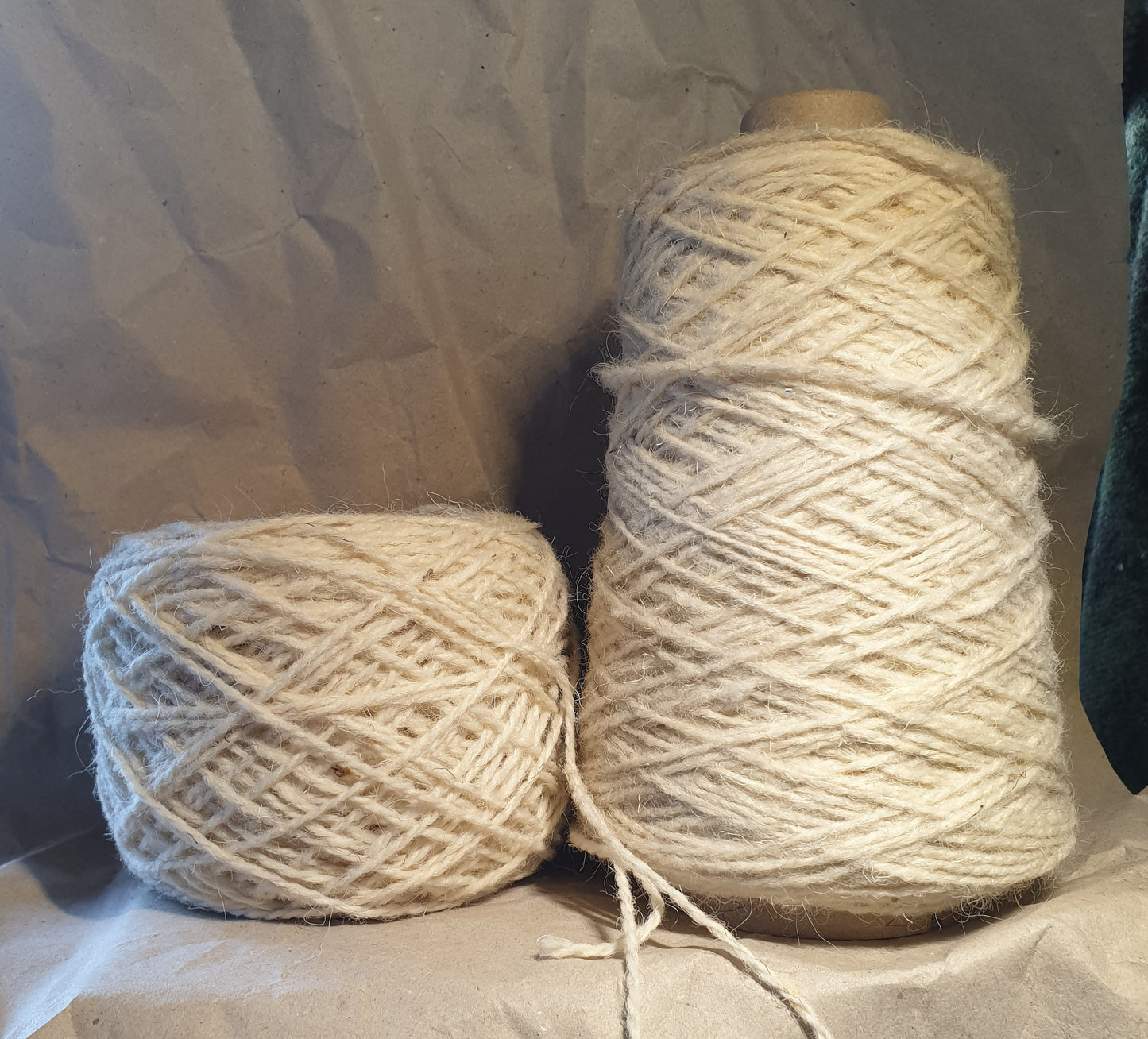 A 100g ball and 250g cone of wool and nylon cream rug yarn