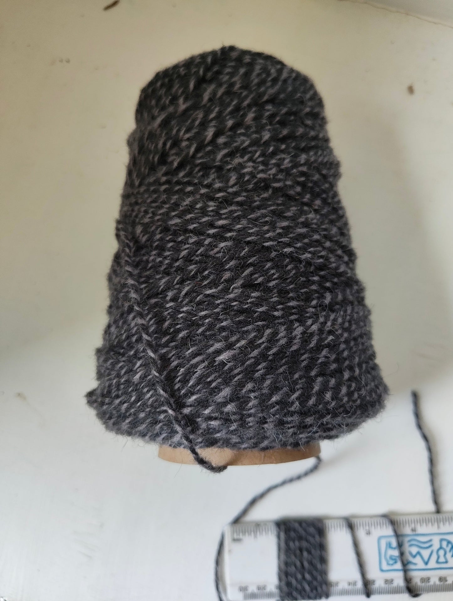 A 250g cone of light and dark grey twisted rug yarns
