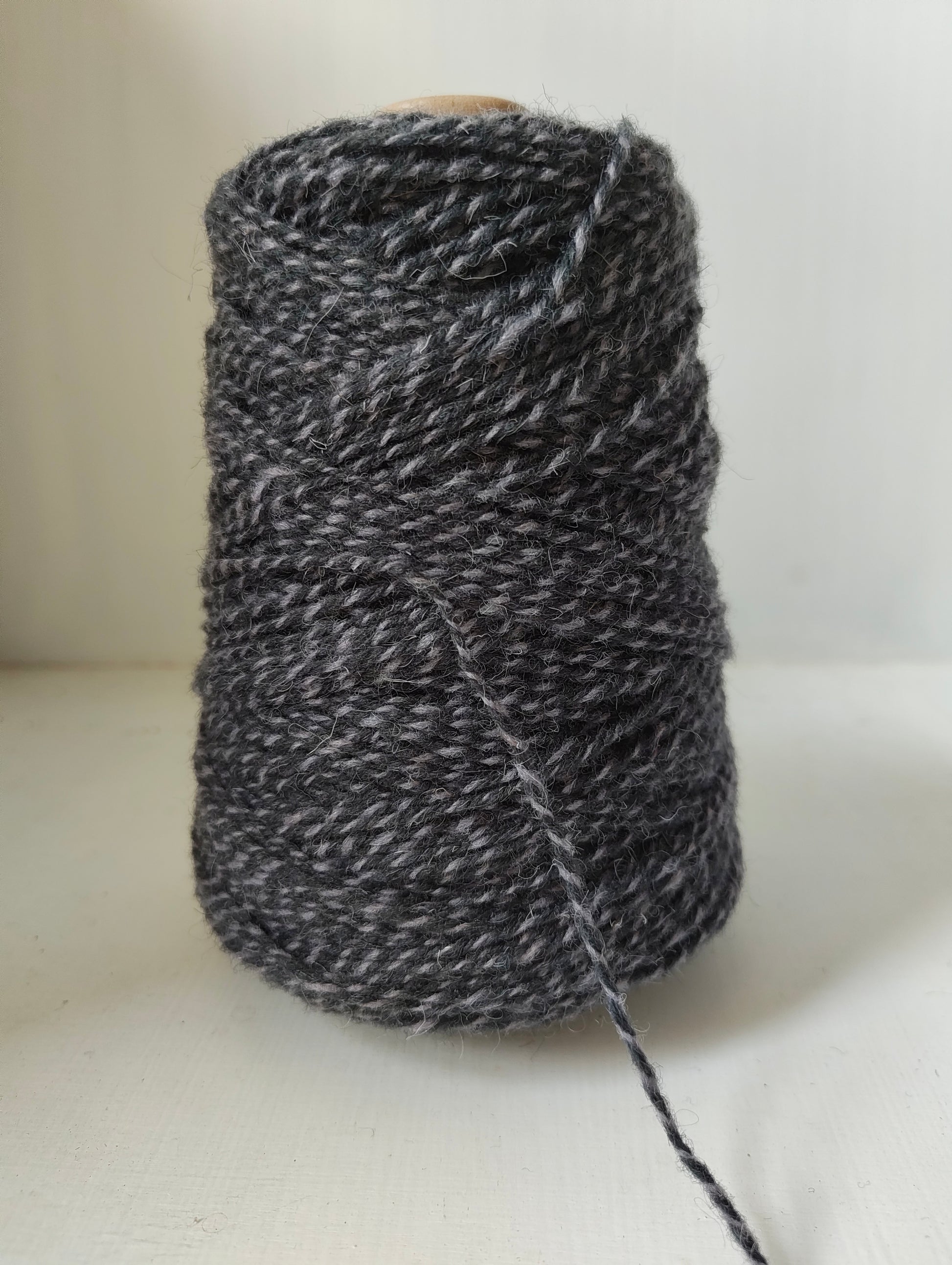A 250g cone of light and dark grey twisted weaving yarns