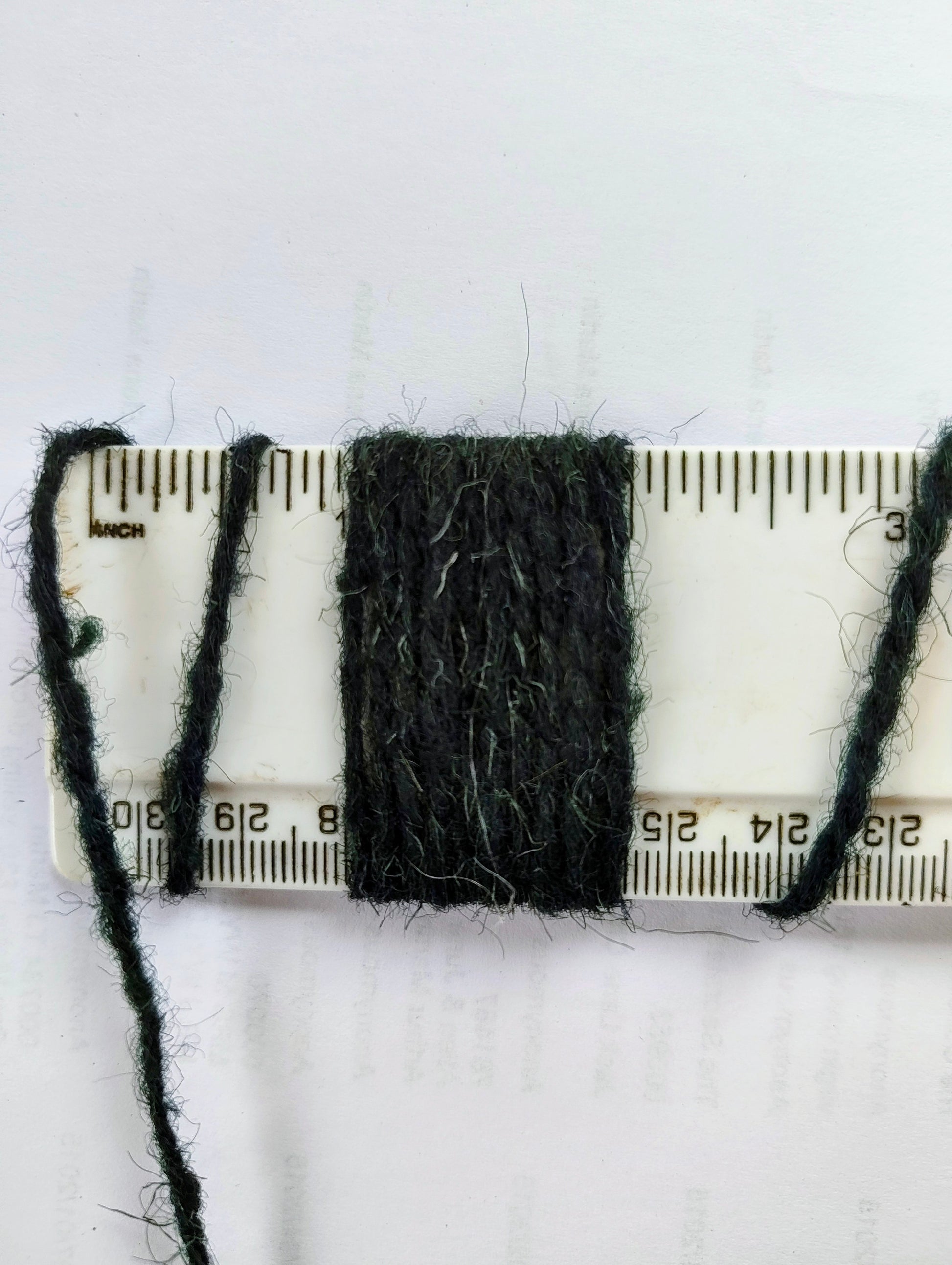 Dark green rug yarn showing 10 wraps per inch