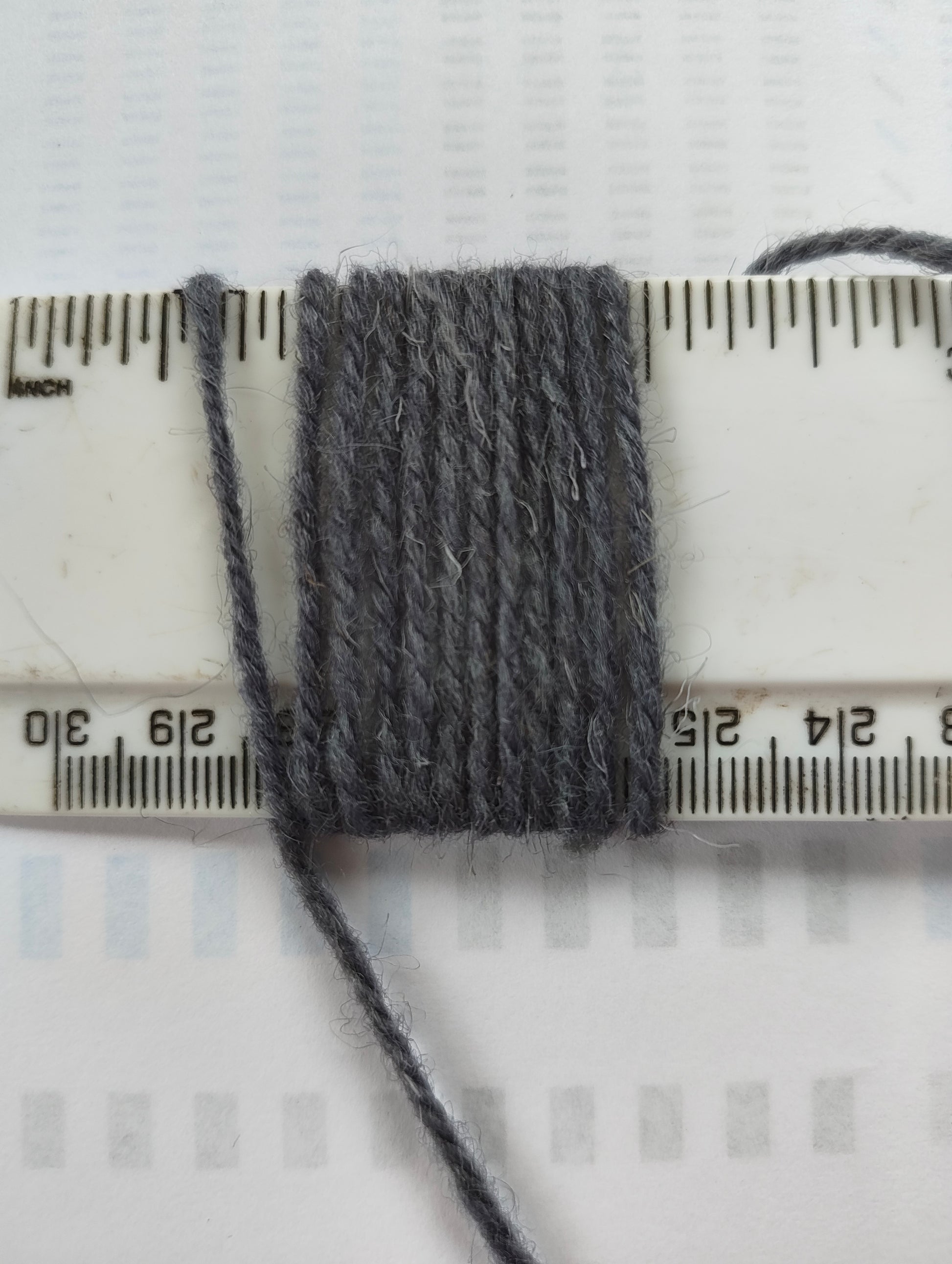 A medium thickness bluey grey rug yarn showing 11 wraps per inch