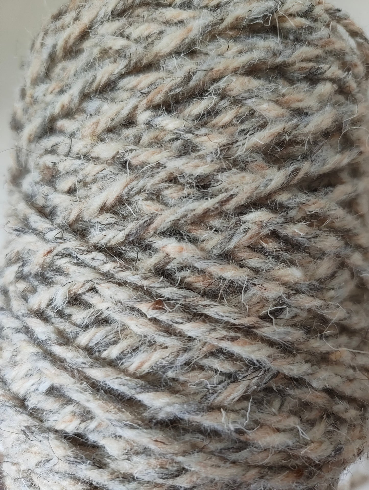 A close up of a thick twisted rug yarn in grey, sand and cream shades