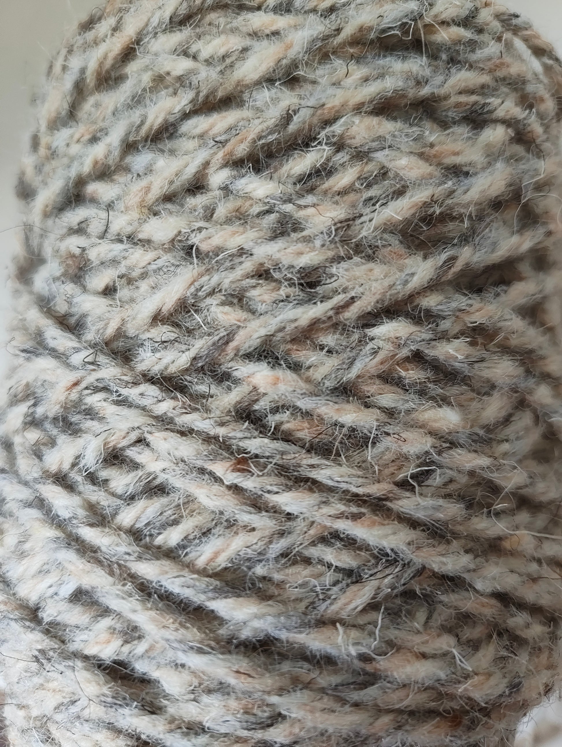 A close up of a thick twisted rug yarn in grey, sand and cream shades