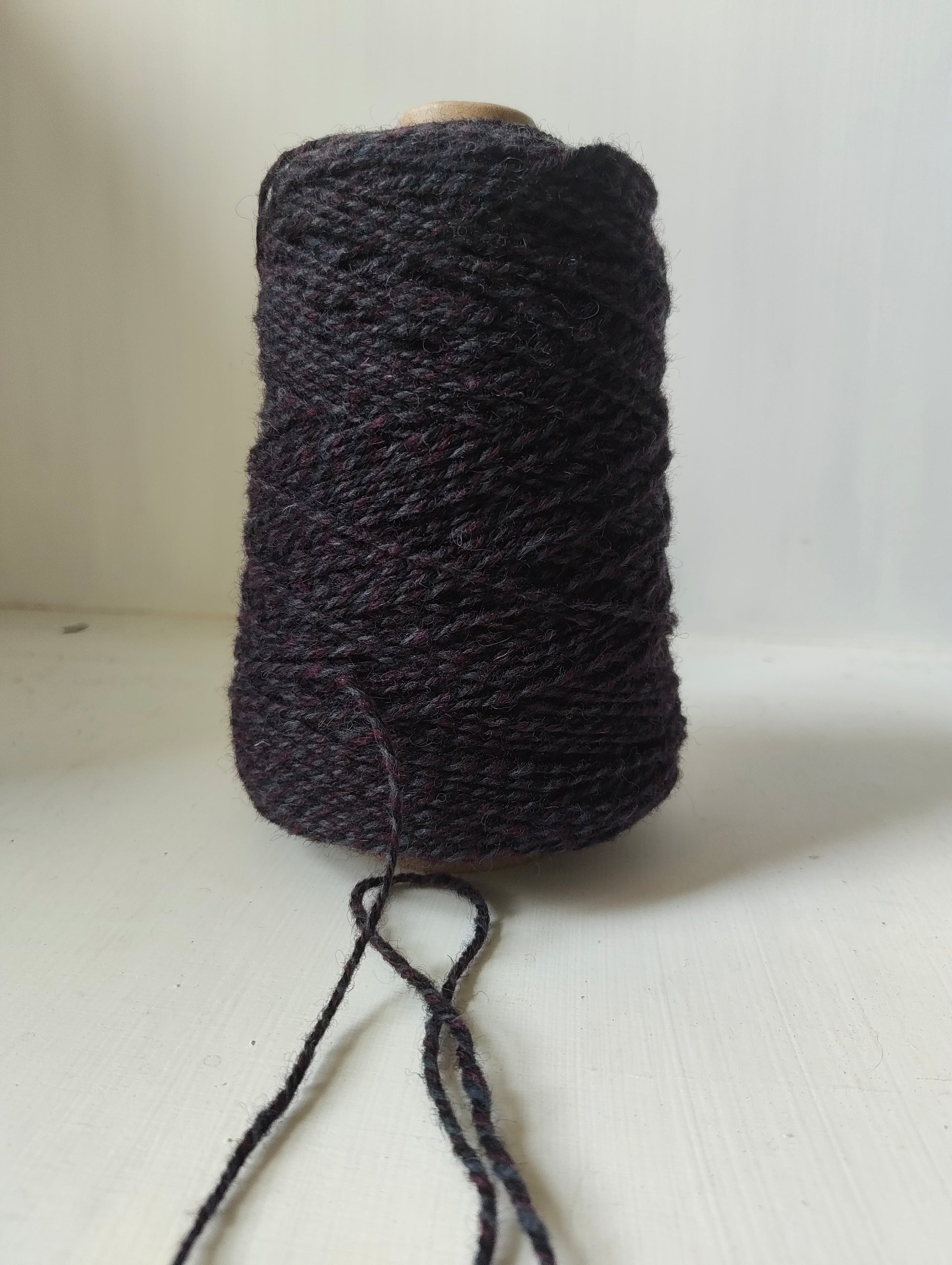 A mix of purple, black and grey rug yarns twisted together on a 250 cone